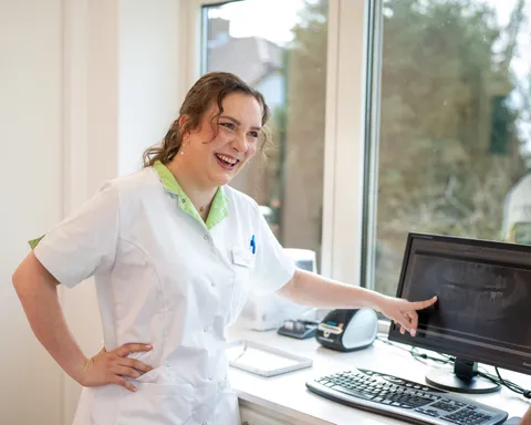 Medewerker lacht breed en wijst een röntgenfoto aan op het scherm