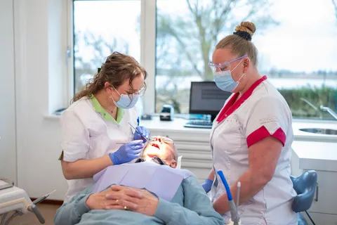 Mondhygiënist polijst de tanden van een patiënt, lichte behandelkamer