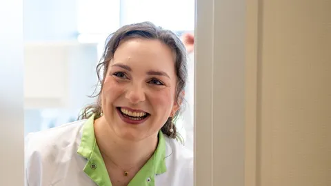 Medewerker kijkt lachend om de hoek van de deur