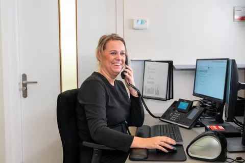 Medewerker van de receptie beantwoordt lachend een vraag aan de telefoon